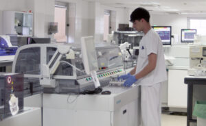 Un facultativo, controlando el flujo de tubos dentro de la cinta automatizada del laboratorio clínico de La Paz.